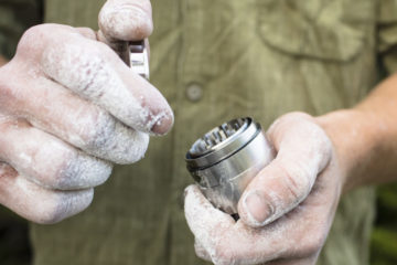 Rock climber holds stainless steel Heady Vermont grinder smoking accessory.